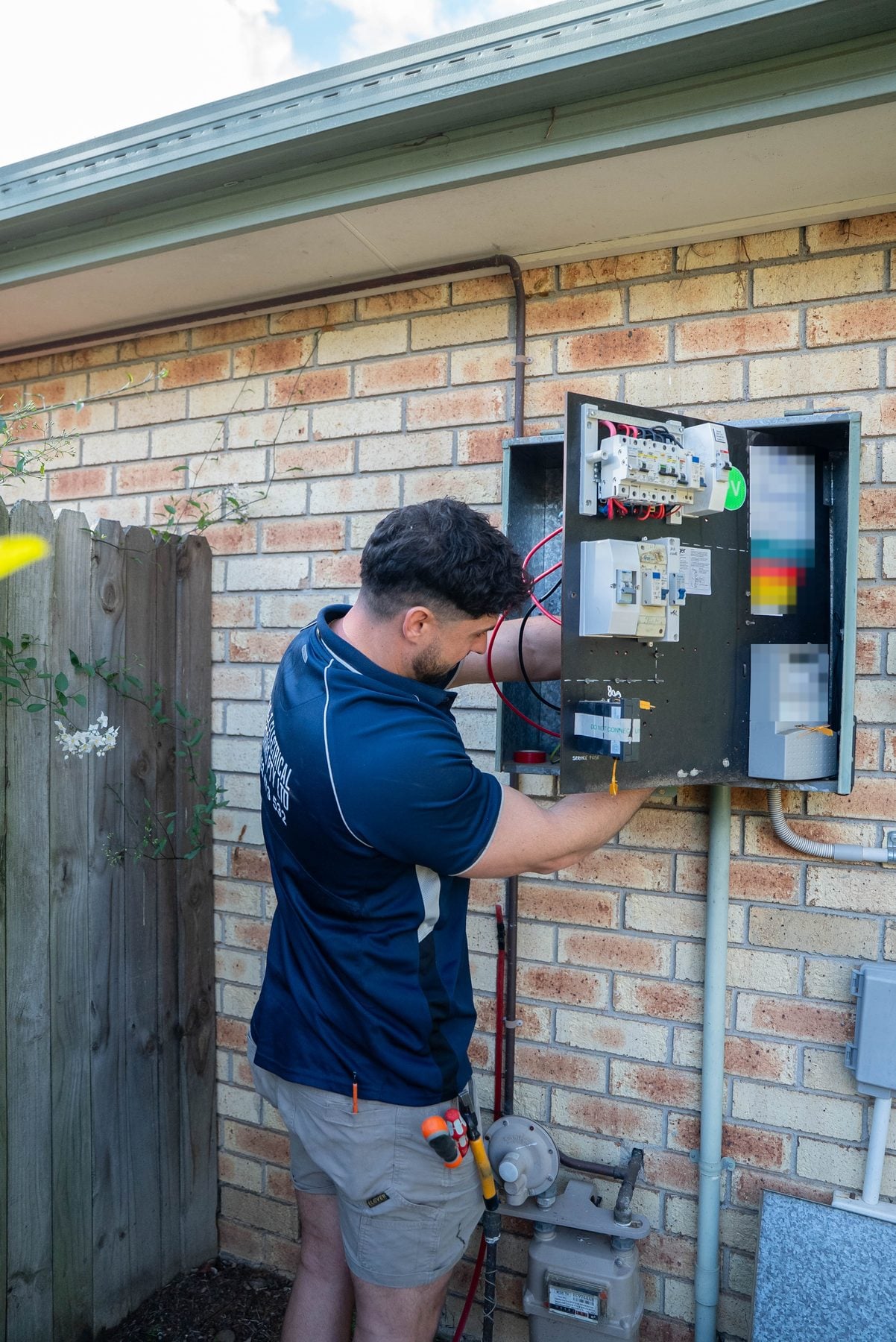 Electrician working inside the open meter box on the brick wall of a Narellan Vale home