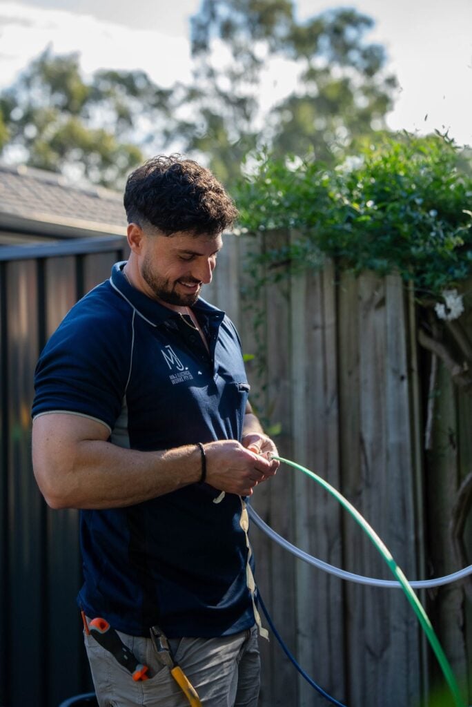 Electrician preparing a coil of cable for the EV charger circuit beside a timber fence in Narellan Vale