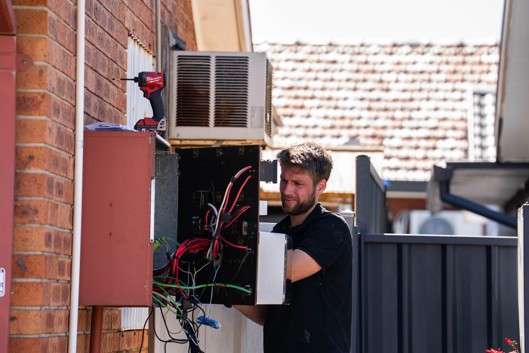 Electrician carrying the old switchboard internals away from a brick wall at a Hoxton Park home