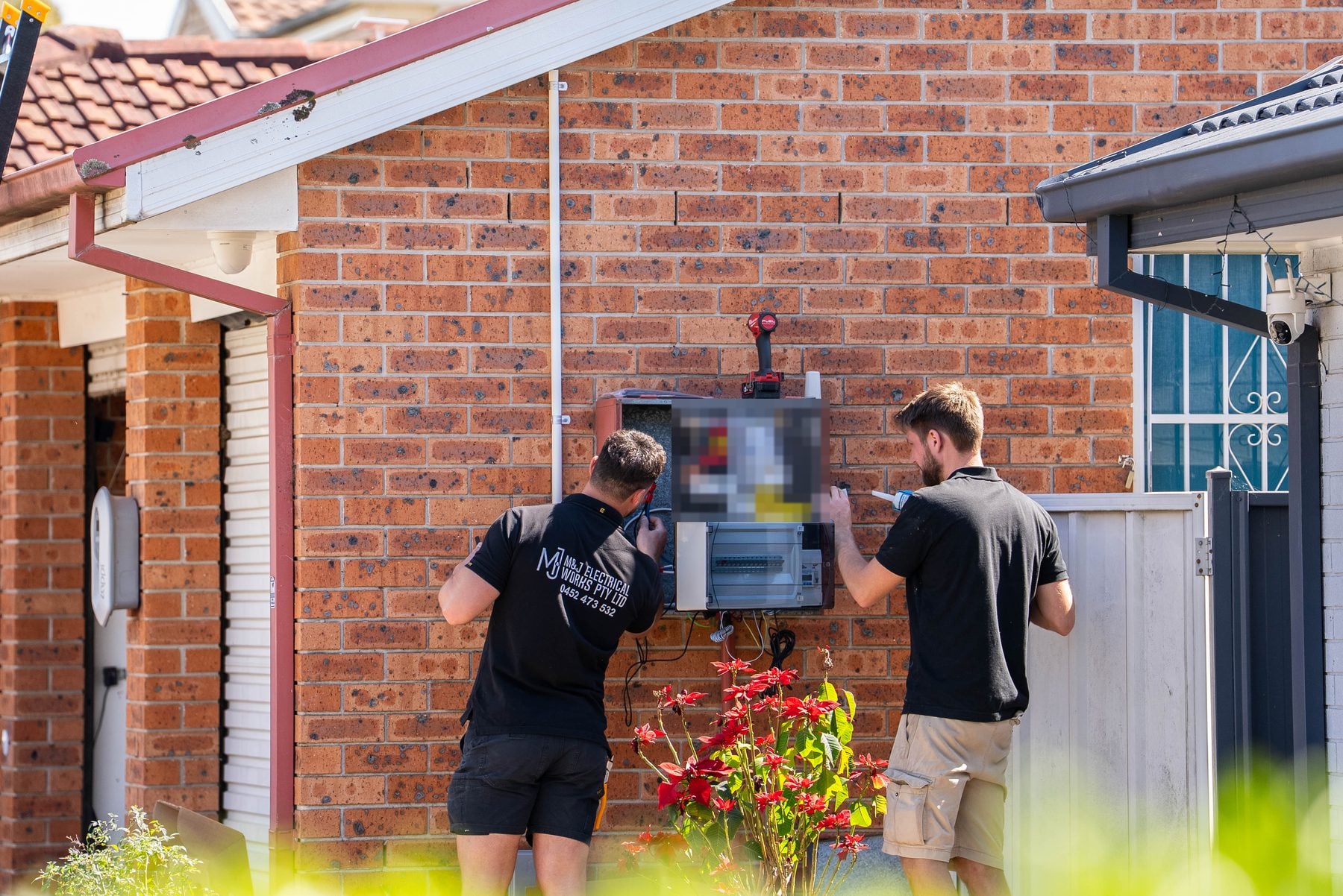 Two M&J electricians finishing a new 18-pole switchboard with individual safety switches on the outside wall of a Hoxton Park home