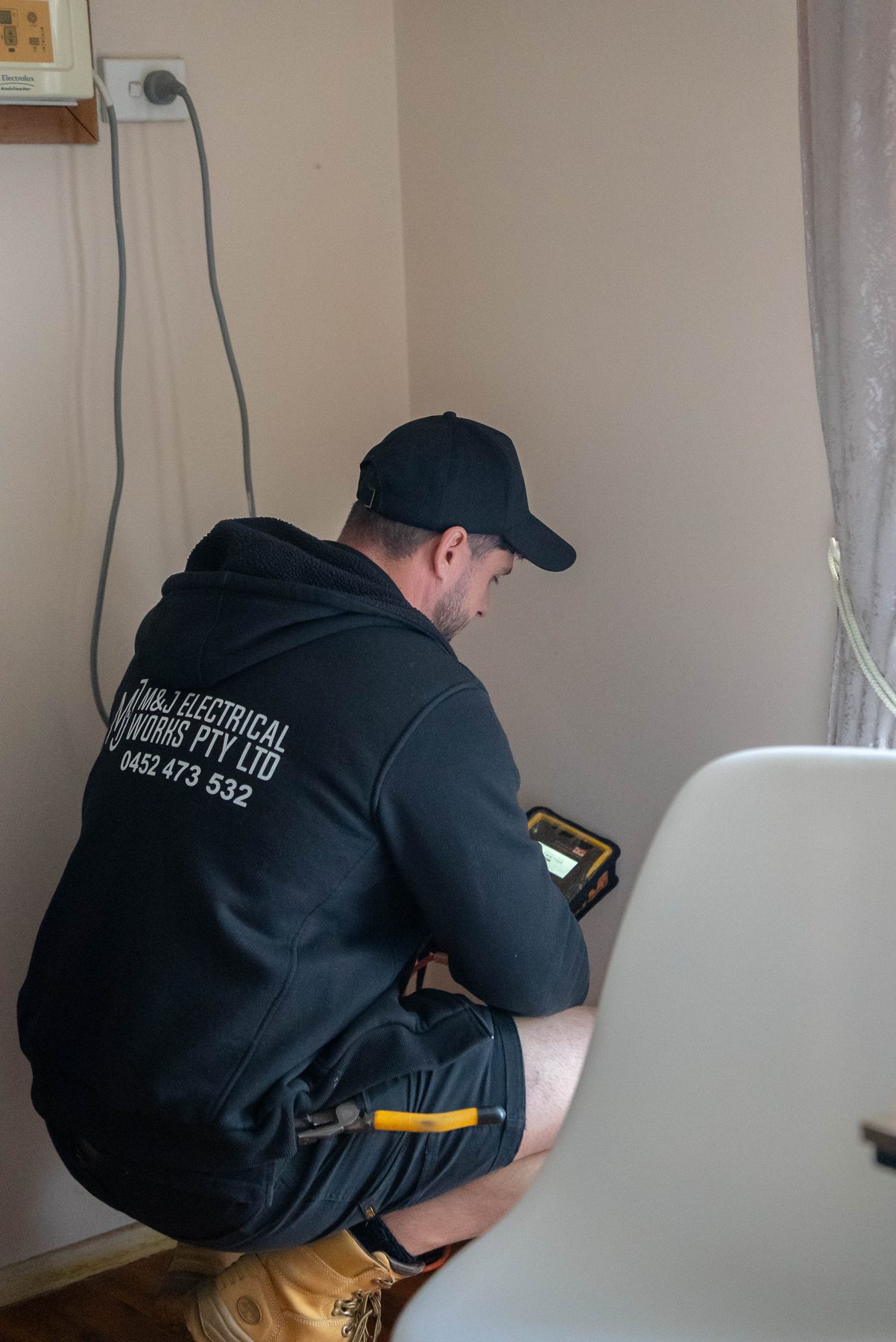 Electrician kneeling to test a power point inside a Leumeah home after a switchboard and consumer mains upgrade
