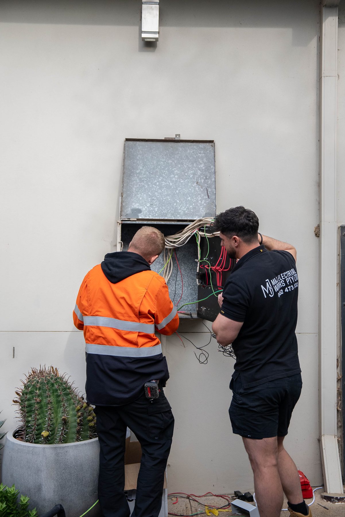 Two electricians working at an open switchboard cavity in a rendered wall during a Camden South renovation