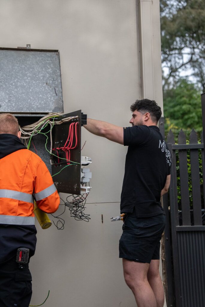 Electrician fitting new switchboard equipment into the enclosure on a rendered wall at a Camden South home