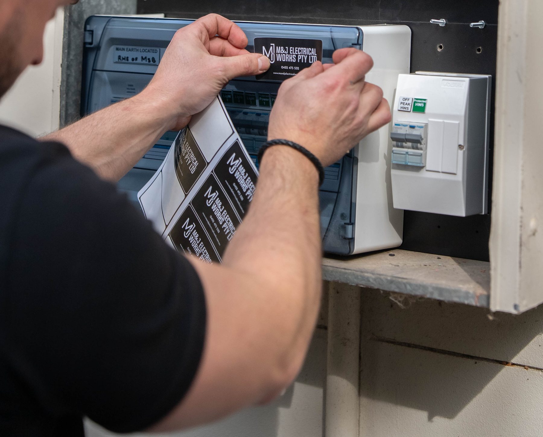 Electrician applying an M&J Electrical Works label to a new Hager switchboard enclosure at a Camden South home
