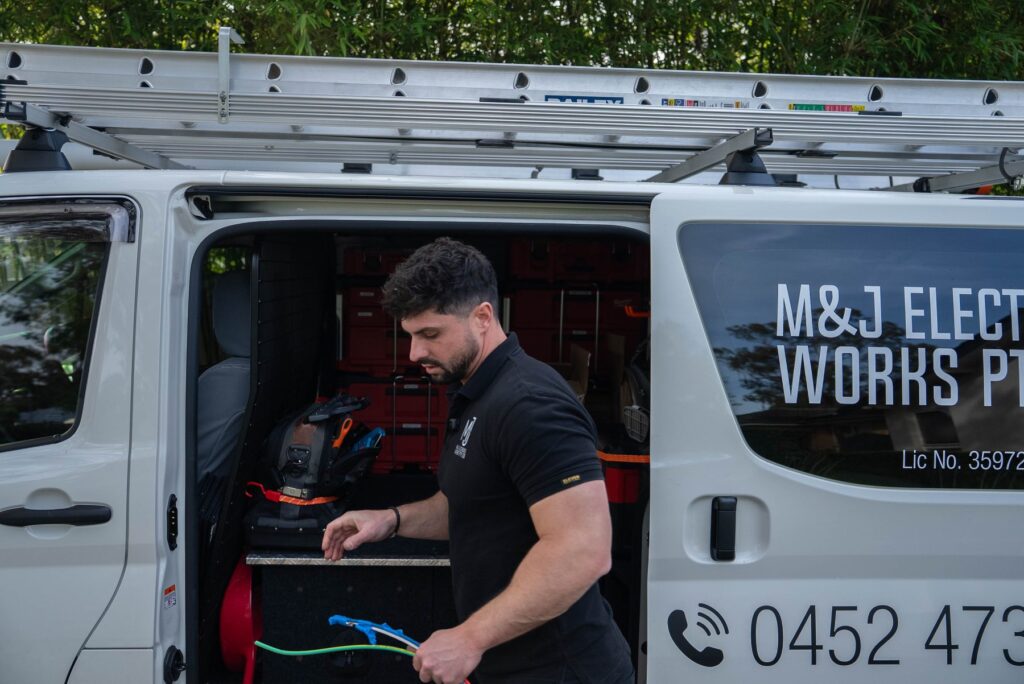 Electrician preparing cable at the open side door of the M&J Electrical Works van outside a Camden South home