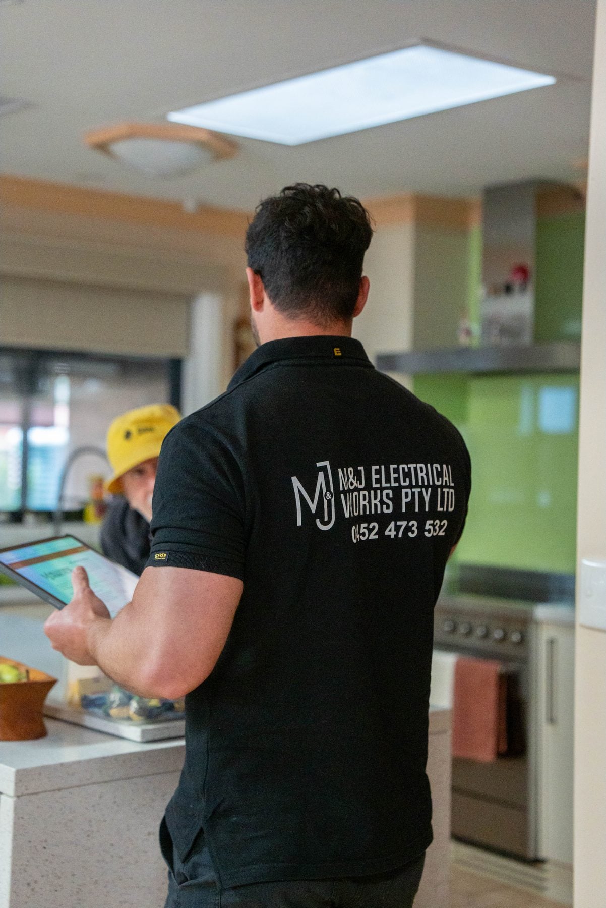 Branded M and J polo as the electrician presents the written quote at the kitchen bench